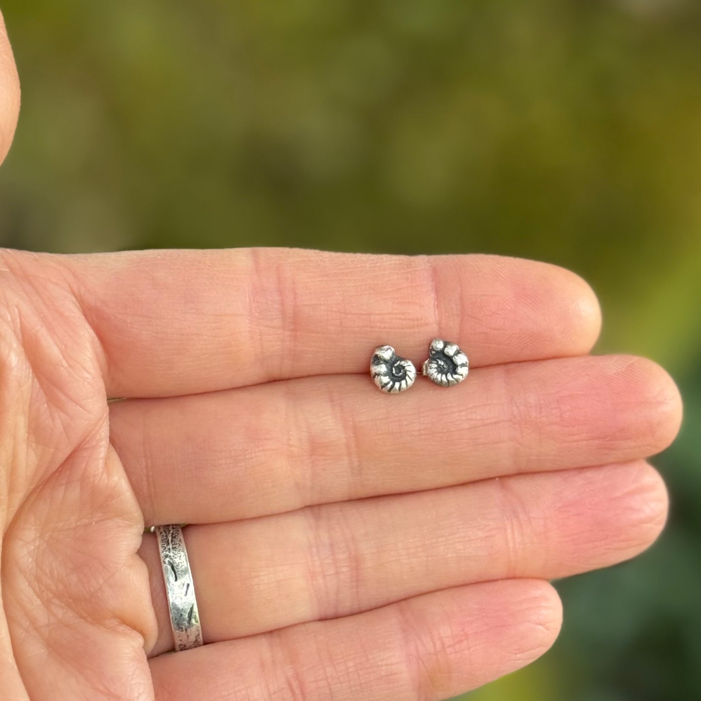 Silver earrings held between fingers with a blurred green background