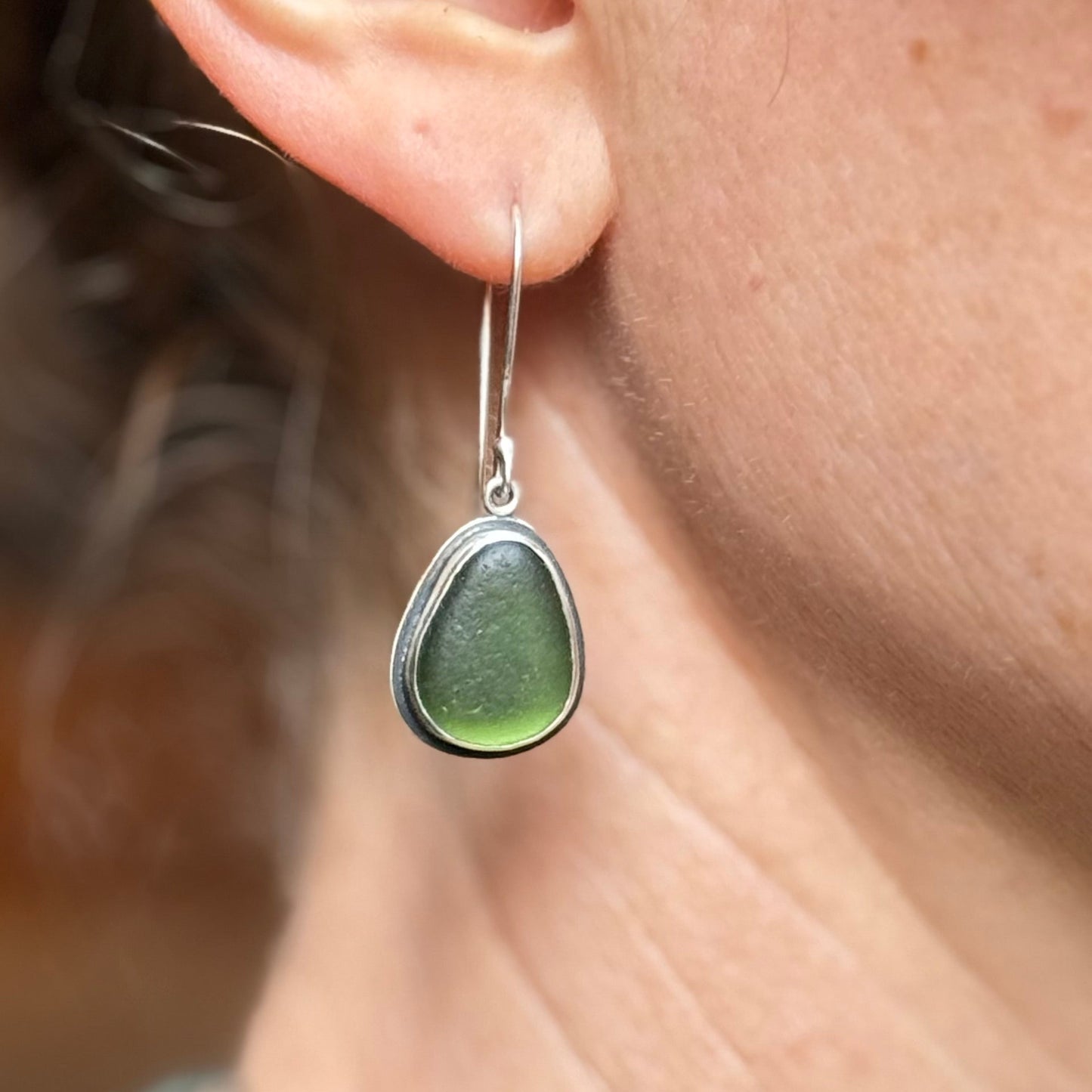 Green teardrop earring on a person's ear with a blurred background