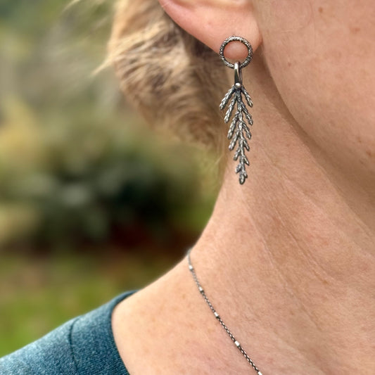 silver cedar leaf earring hanging from an earlobe