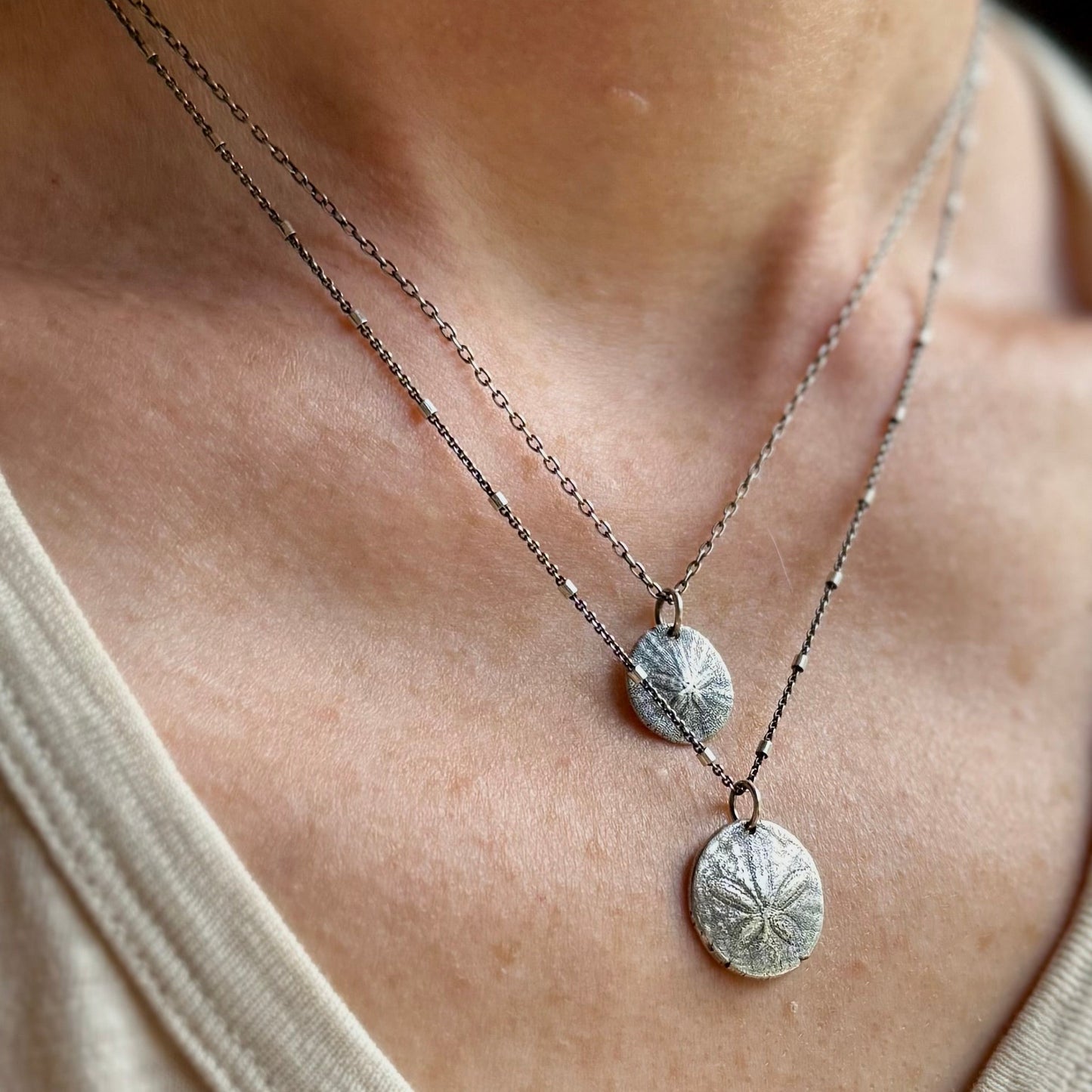 Close-up of a person wearing a silver necklace with sterling silver sand dollar pendants.